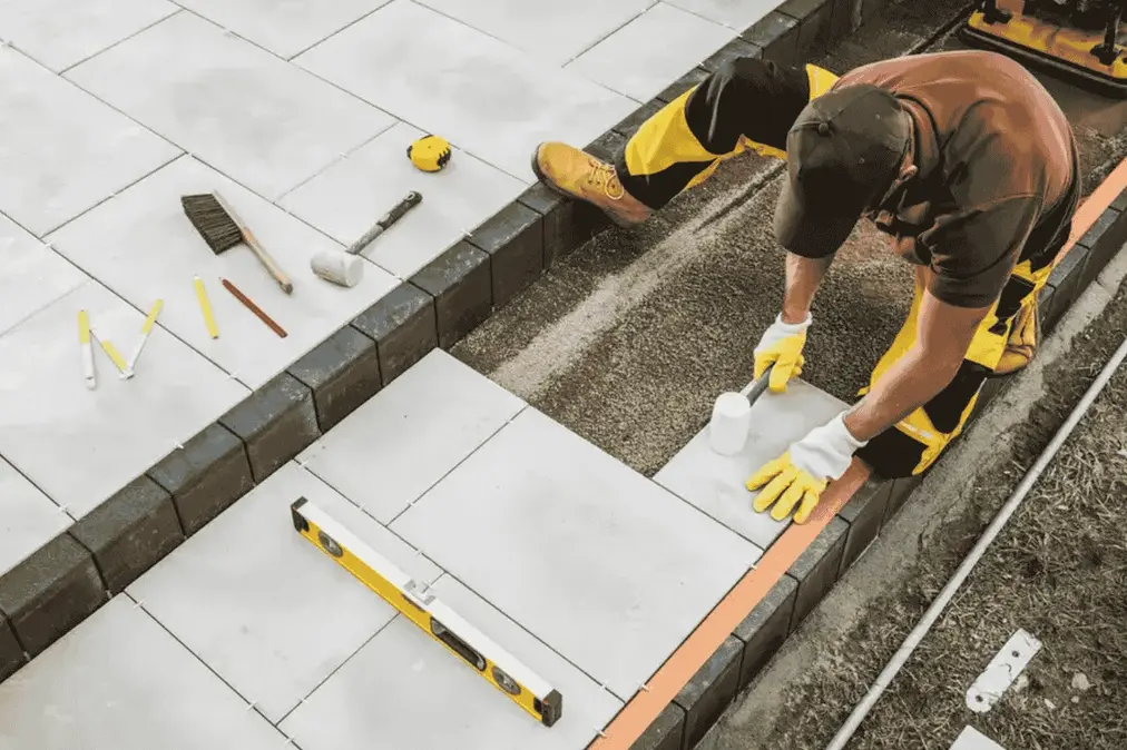A bricklayer placing down a large stone brick into a footpath he is building. He is using a mallet to precisely position it.