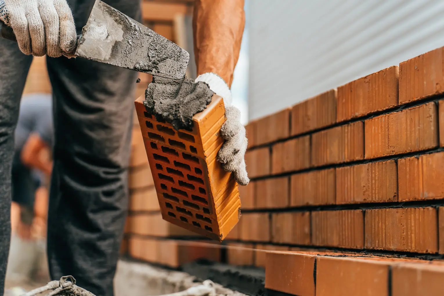 Close up of a bricklayer wiping cement onto a brick before they place it on a wall