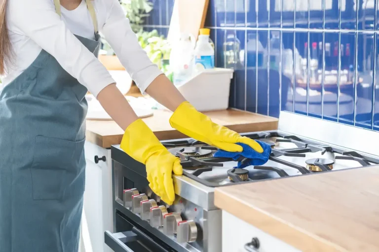 Close up of a person cleaning an oven for a client. They are wearing bright yellow gloves.